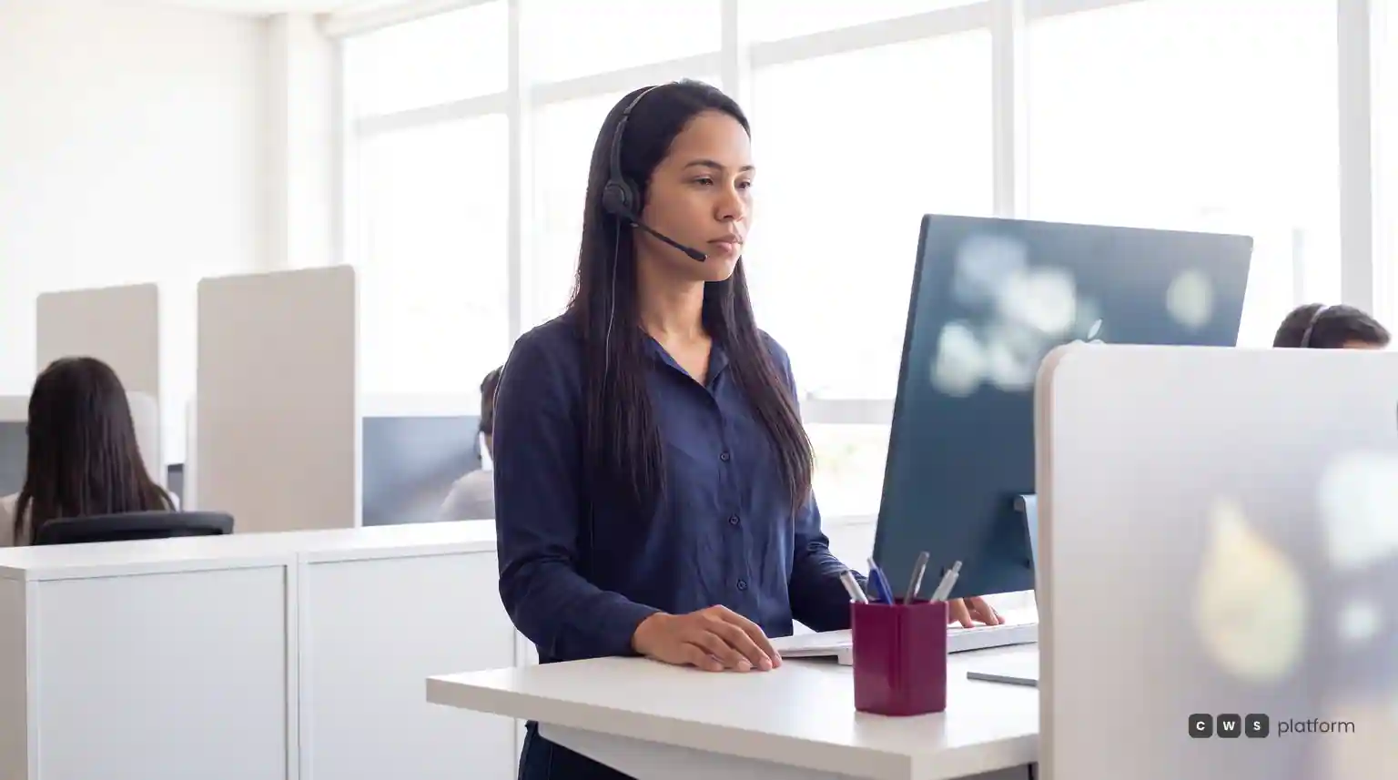 Atendente com headset em uma estação de trabalho, olhando para o monitor em uma central de atendimento.